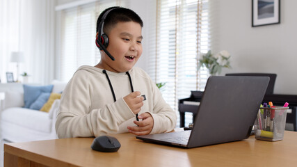 Young asia boy student wear headset headphone with computer laptop videocall talk present online e-learning class study with teacher, social distance learn language at home, homeschooling concept.