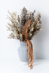 Stylish modern boho dried flower arrangement in a cream and blue stripe vase. Including Native Temp, Ruscus leaves, Stirlingia, Parchment Fern and Amaranthus. Photographed on a white background.
