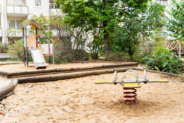 Modern multi-colored playground with slides, swings and other children's attractions on the sand in the courtyard with green trees on a summer day