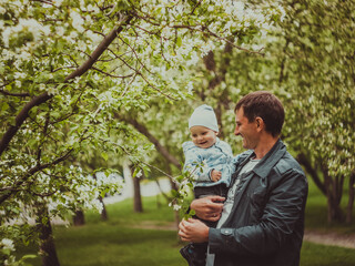 Small cute baby boy with his father walking in spring park outdoor. Man hold his little son on hands. Blooming trees in the garden. Smile and parent care