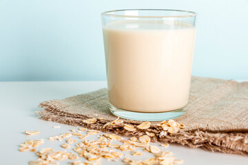 Glass of oat vegetable milk and scattered oat flakes on table. Concept of making plant based organic veggie Milk, lactose free. Healthy Nutrient Breakfast.