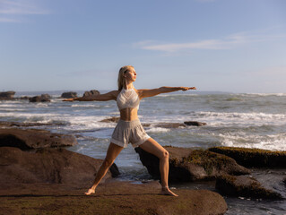 Fototapeta na wymiar Young woman practicing yoga. Standing in Virabhadrasana II pose, Warrior II Pose. Work out. Healthy lifestyle. Strong body. Ocean background. Yoga retreat. Self-care concept. Beach in Bali