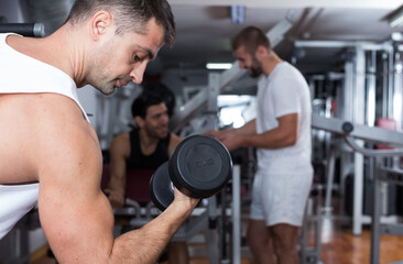 Fototapeta na wymiar Muscular young man doing exercises with dumbbells at gym