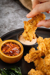 Woman holding tasty Fried chicken and bowl with sauce on table, closeup