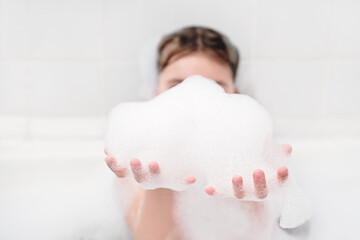 girl playing with bath foam in the bathroom. little girl making froth and holding it in hands. kids hygiene, evening routine