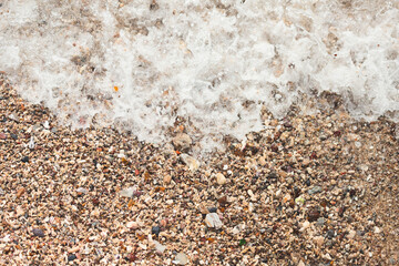 A sandy beach with foam from the waves crashing into the shore.