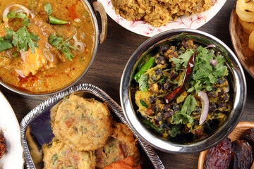 Bengali Iftar Ramadan breakfast spread ripe dates peep fried spicy piaju onion fitter eggplant tanpura potato chop haleem jilapi khichuri rice chana sola curry on rustic wooden table