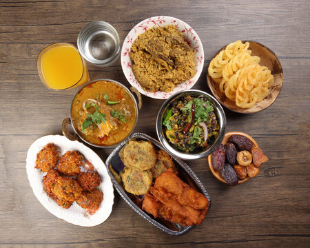 Bengali Iftar Ramadan breakfast spread ripe dates peep fried spicy piaju onion fitter eggplant tanpura potato chop haleem jilapi khichuri rice chana sola curry on rustic wooden table