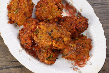 Deep fried piaju onion fitter bhajia on decorated ceramic plate over rustic wooden background