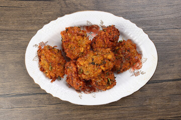 Deep fried piaju onion fitter bhajia on decorated ceramic plate over rustic wooden background