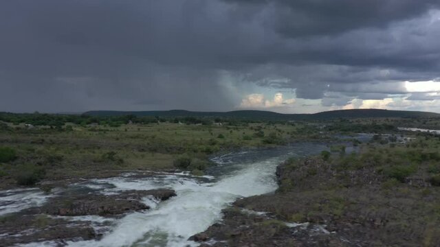 Aerial over rapids and river with green vegetation, hills and storm clouds in the background, Zambia. 
