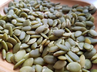 Green pumpkin seeds lie on a wooden plate