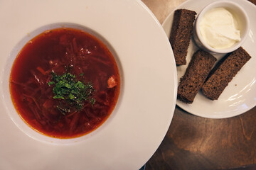 A traditional dish of Russian and Ukrainian cuisine. Borscht with herbs, sour cream and garlic croutons. On a wooden table with copy space