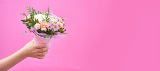 Beautiful bouquet of mixed different flowers in hand on pink background banner with copy space, greeting, gift