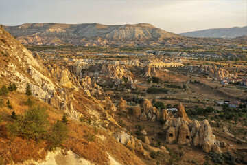 The magnificent landscape of Cappadocia at golden hour. In the valley, surrounded by beautiful mountains, one can see unusual pointed rocks with caves, rural houses. Turkey