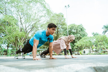 a young man and a girl in a headscarf doing movement to train chest muscles together when outdoor exercise in the park