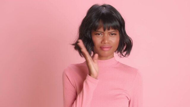 Unhappy dissatisfied dark skinned woman waves palm near nose smells unpleasant stench dressed in casual wear poses over pink background sees something disgusting. Avoiding bad smell, nasty feelings.