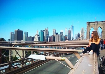 a woman posing on the Brooklyn Bridge and with the skyline of Manhattan, New York in the background