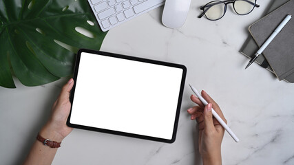 Woman hand holding mock up digital tablet with blank screen and stylus pen on marble background.