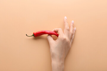 Female hand with chili pepper on color background. Erotic concept
