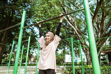 a girl in veil doing pull up to improve lung ability and lose weight by exercising outdoors in the park