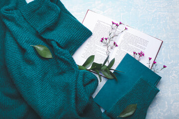 Books with fresh flowers and sweater on color background