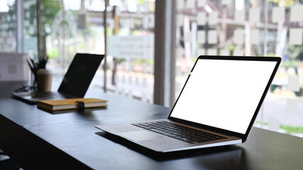 Close up view of computer laptop with blank screen on black wooden table in office room.