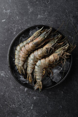 raw black tiger prawns on ice on a black background, top view, selective focus
