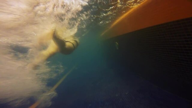 Underwater view of a girl in swimming suit swimming in cloudy pool water.