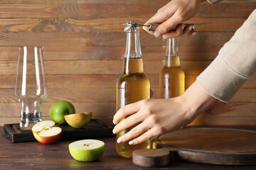 Woman opening bottle with cold cider on wooden background