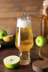 Woman pouring cold cider from bottle into glass on wooden background