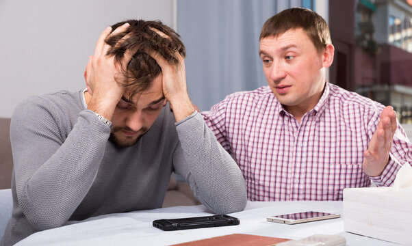 Man comforting his upset friend while discussing problems at table at home
