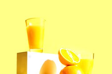 Fresh and juicy orange juice in glasses on trendy white catwalks with hard shadows on a yellow background. Healthy food and drink concept. Copy space