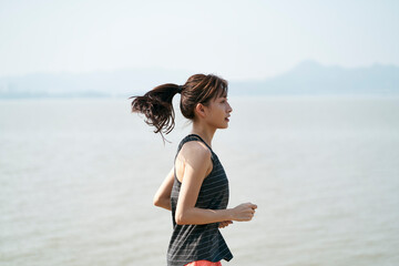 young asian woman runner running outdoors by the sea