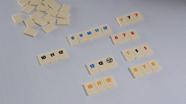 Two players are playing the board game rummikub on a white table. Tiles are laid out one by one