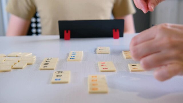 Two players are playing the board game rummikub on a white table. Tiles are laid out one by one