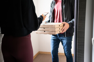 Pizza delivery phone app concept. Food deliverer at home door and customer using cellphone to pay,...