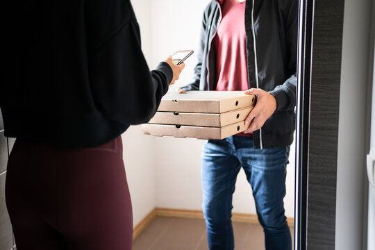 Pizza delivery phone app concept. Food deliverer at home door and customer using cellphone to pay, tip or give online rating and review to business. Fast food boxes of an Italian restaurant.
