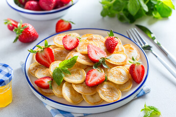 Morning mini pancakes in a white plate with fresh strawberries, horizontal