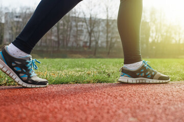 Woman runner sprinting on a treadmill in a stadium, outdoors. Close-up of female legs in sports jogging shoes. Active lifestyle