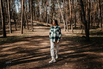 A pregnant woman in a shirt and white pants walks in the forest.