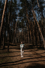 A pregnant woman in a shirt and white pants walks in the forest.