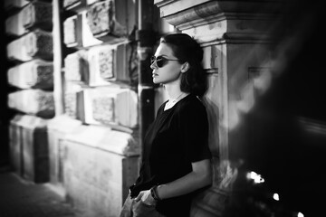 Black and white portrait of stylish young woman in sunglasses sitting in profile