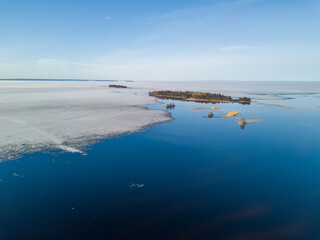 Aerial view of the large Onega Lake in Karelia (northwest Russia) with melting ice and big area of open water near the coast and the island. Forest by the lake. Sunny, spring day