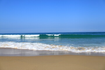 Fototapeta na wymiar Une vague avec de l´écume blanche déferle vers la plage de sable , il fait beau, le ciel est bleu.