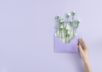 Minimal newsletter email concept with hand holding a violet envelope with white summer flowers on bright purple background. Send message creative idea. Purple aesthetic with copy space.