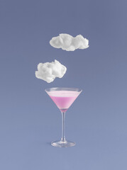 Minimal summer dream concept with martini glass pink cocktail drink and dreamy clouds on violet purple background. Fashion, party, dreaming creative idea with copy space.