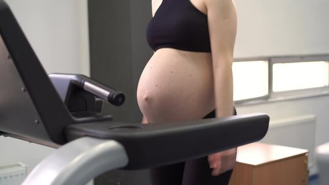 Pregnant Woman training treadmill machine in gym Cardio exercises on running simulator Run walking Healthy lifestyle Sport and fitness concept. Caucasian female pregnancy workout