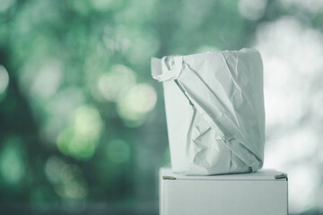 Small glass wrapped in white paper placed on white box against nature background.