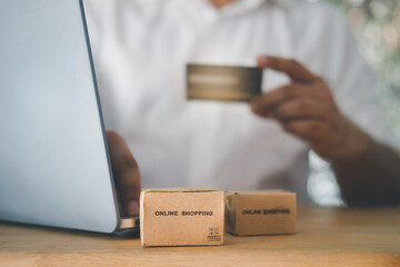 Man holding black credit card in hand and online shopping using on laptop at home with brown box.